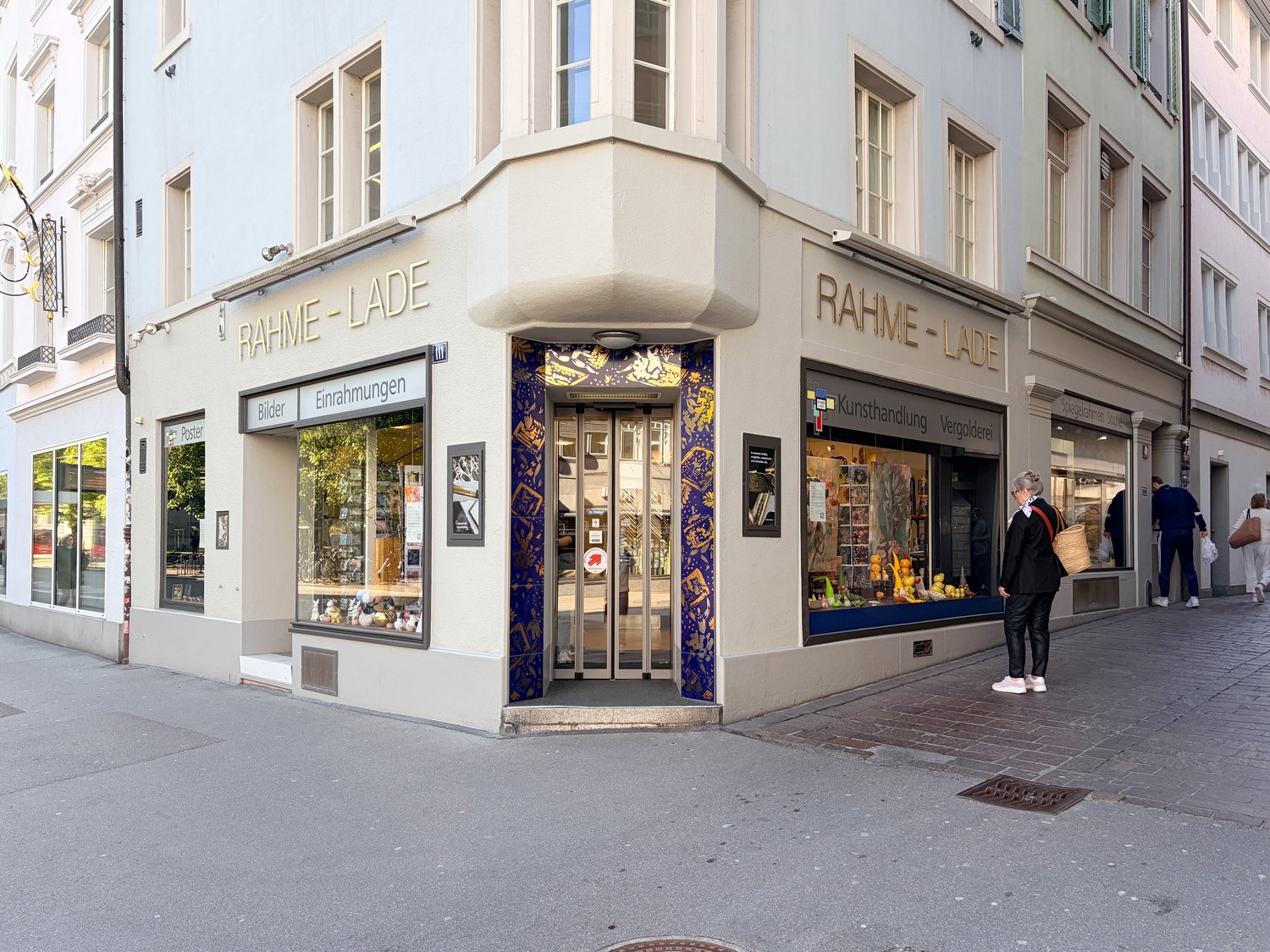 Facade of a building with glass windows and doors, name Rahme-Lade, people walking on the sidewalk