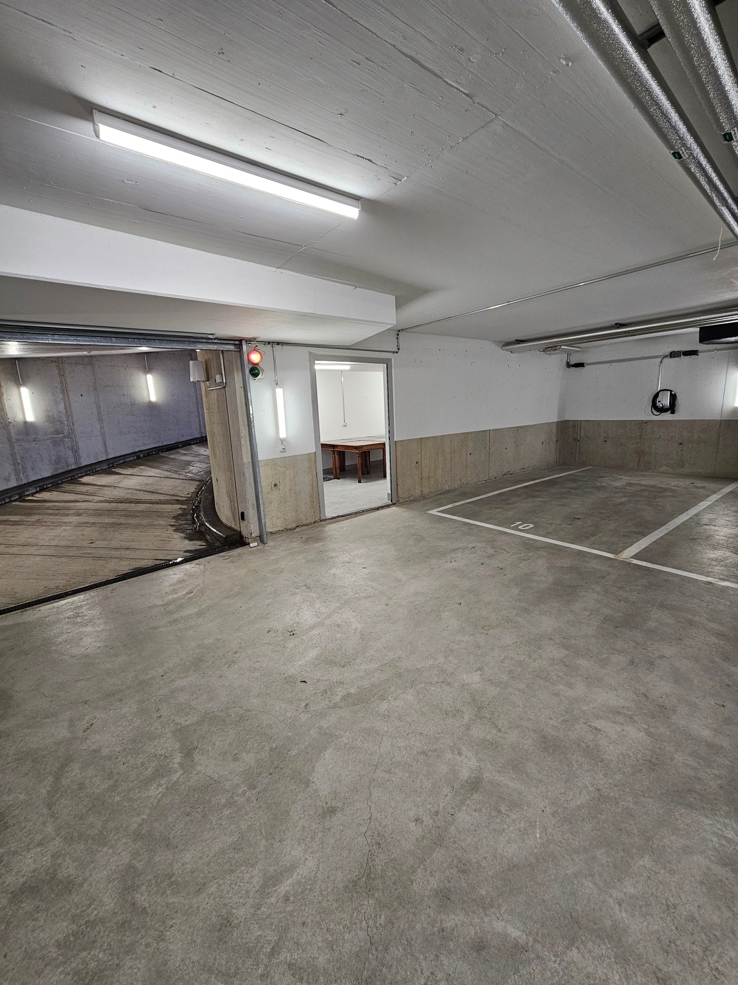 underground parking garage, concrete floor, white and grey walls, ceiling lights, numbered parking spots, central open area