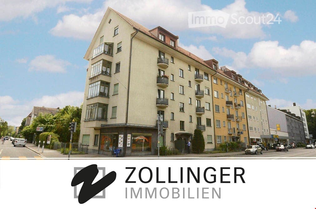 Multi-story building, yellow exterior, glass windows, multiple balconies, street with parked cars and streetlights, greenery, clear sky with clouds
