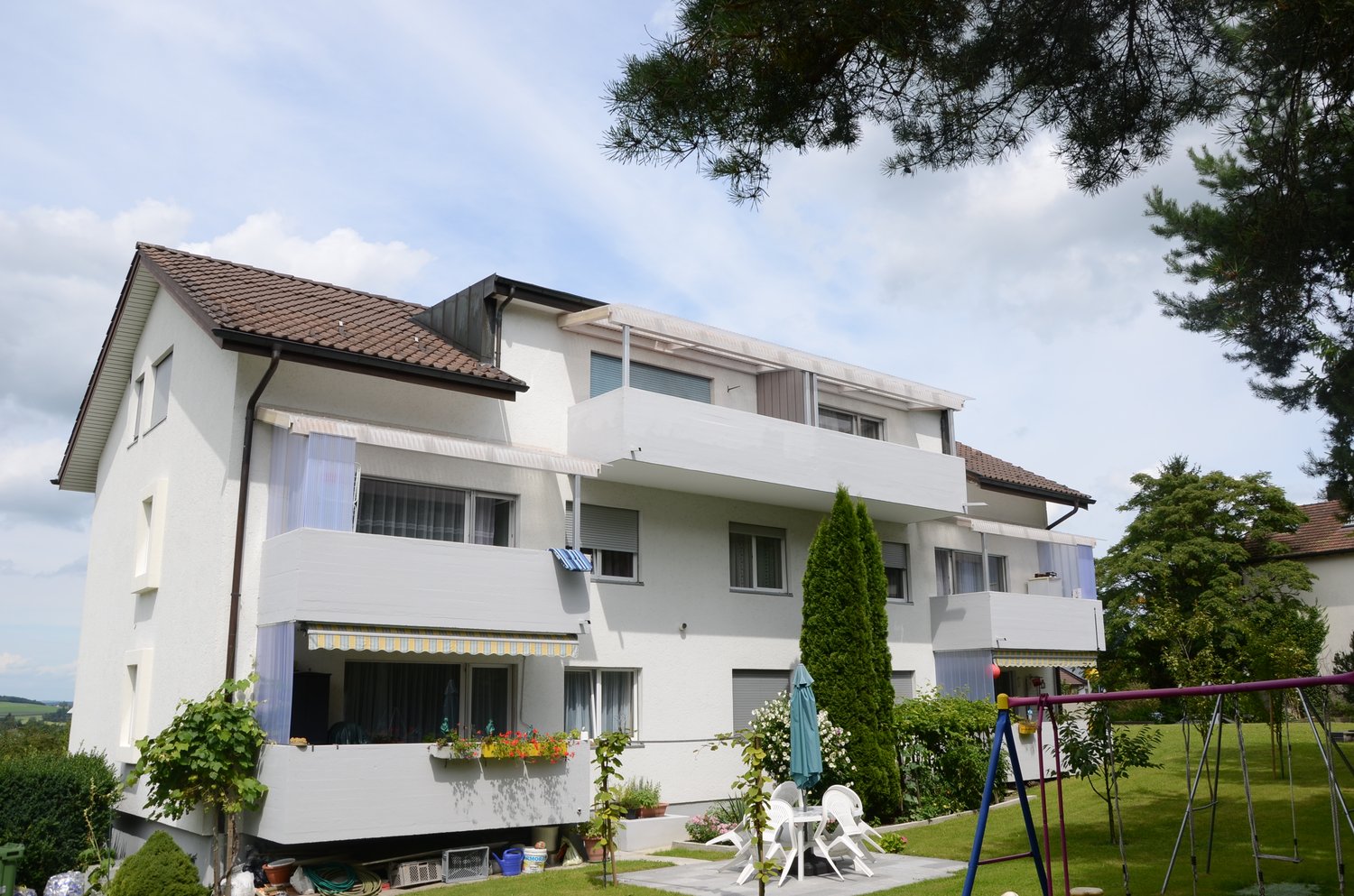A multi-story apartment building with a white exterior, balconies, and a well-maintained garden area with a children's playground.