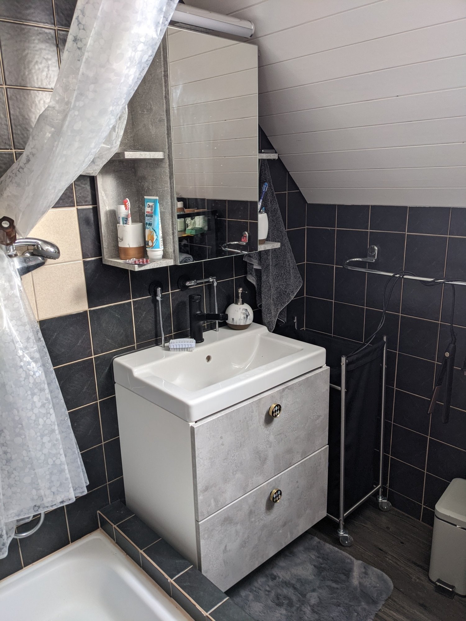 Bathroom with tiled walls and wooden floors, featuring a sink with a cabinet, a bathtub, a shelf above the sink, and a towel rack.