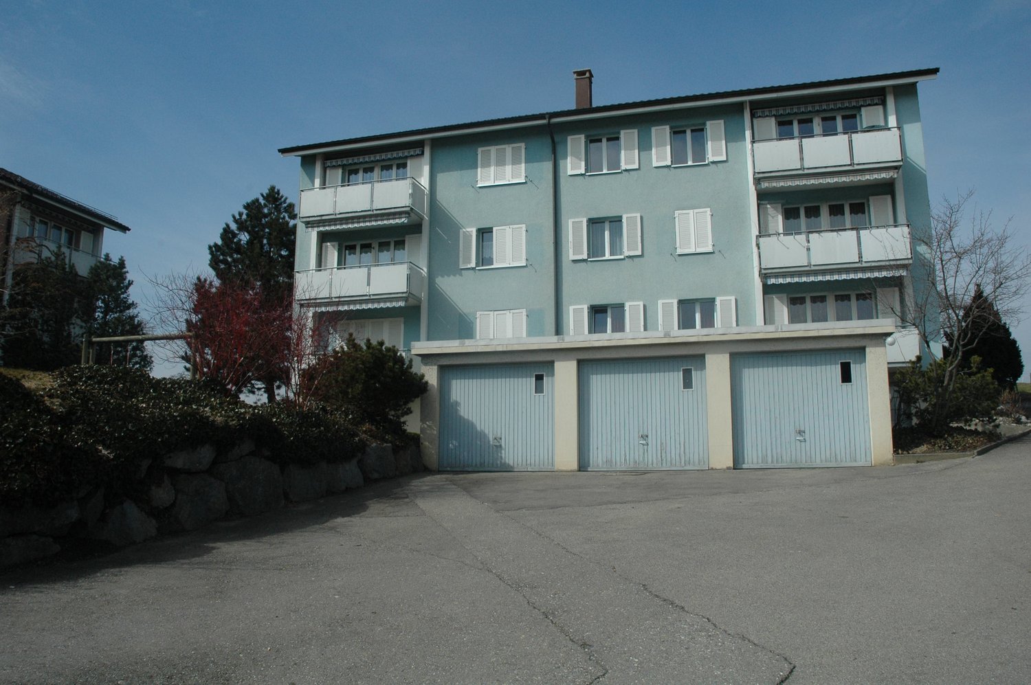3 story building, white shutters, balcony, blue exterior, stone driveway, 3 garages