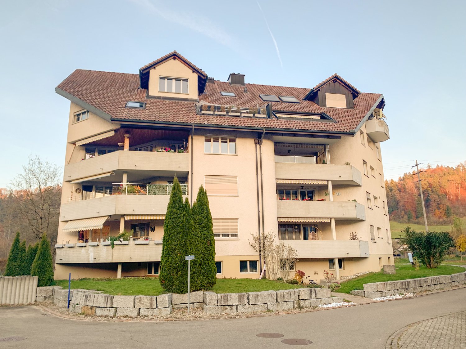 Multi-story apartment building, multiple balconies, brick facade, solar panels on roof, raised ground floor
