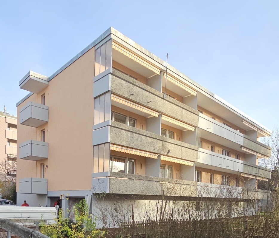 Apartment building with multiple balconies, multiple windows, red roof, beige walls