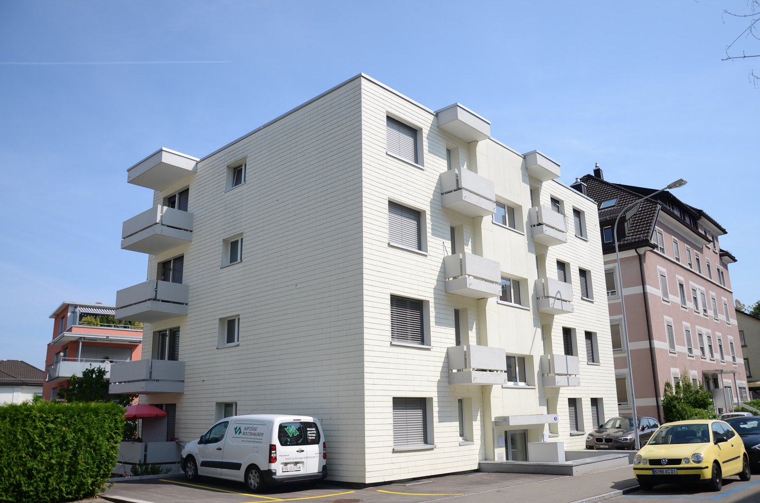 3-story apartment building, white facade, balconies, two cars parked in front