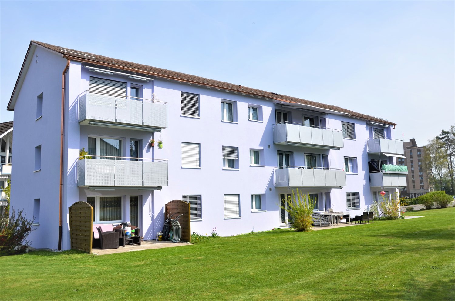 3 story apartment building, white exterior, brown roof, multiple balconies, large lawn in front