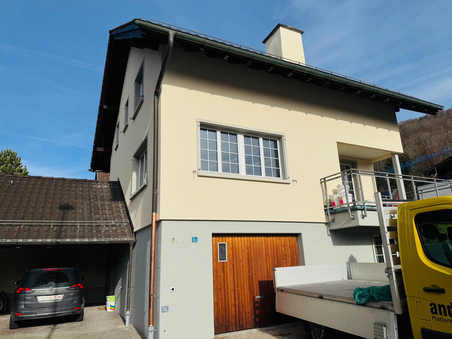 Detached house, beige walls, glass windows, wooden door, brown roof, single garage, chimney, balcony with railings
