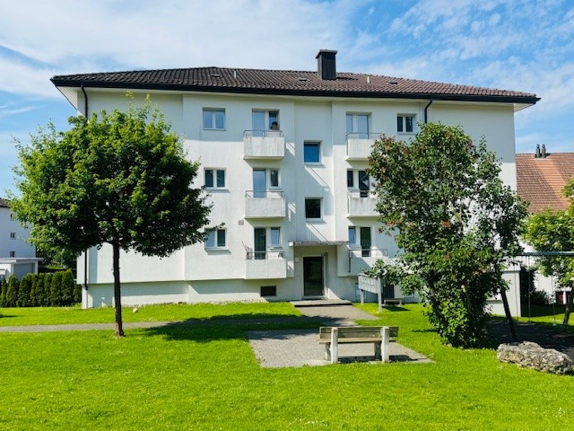 Multi-story apartment building, balconies, entrance, trees, grass, bench