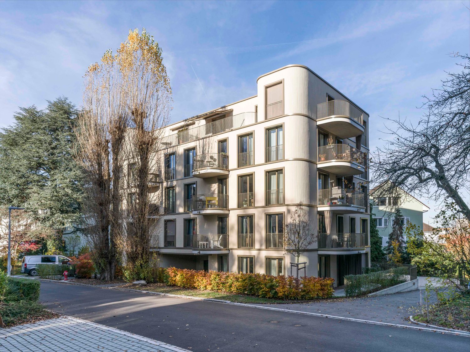 Modern 6-story apartment building, white exterior, balconies on each floor, modern architecture, paved parking area, greenery