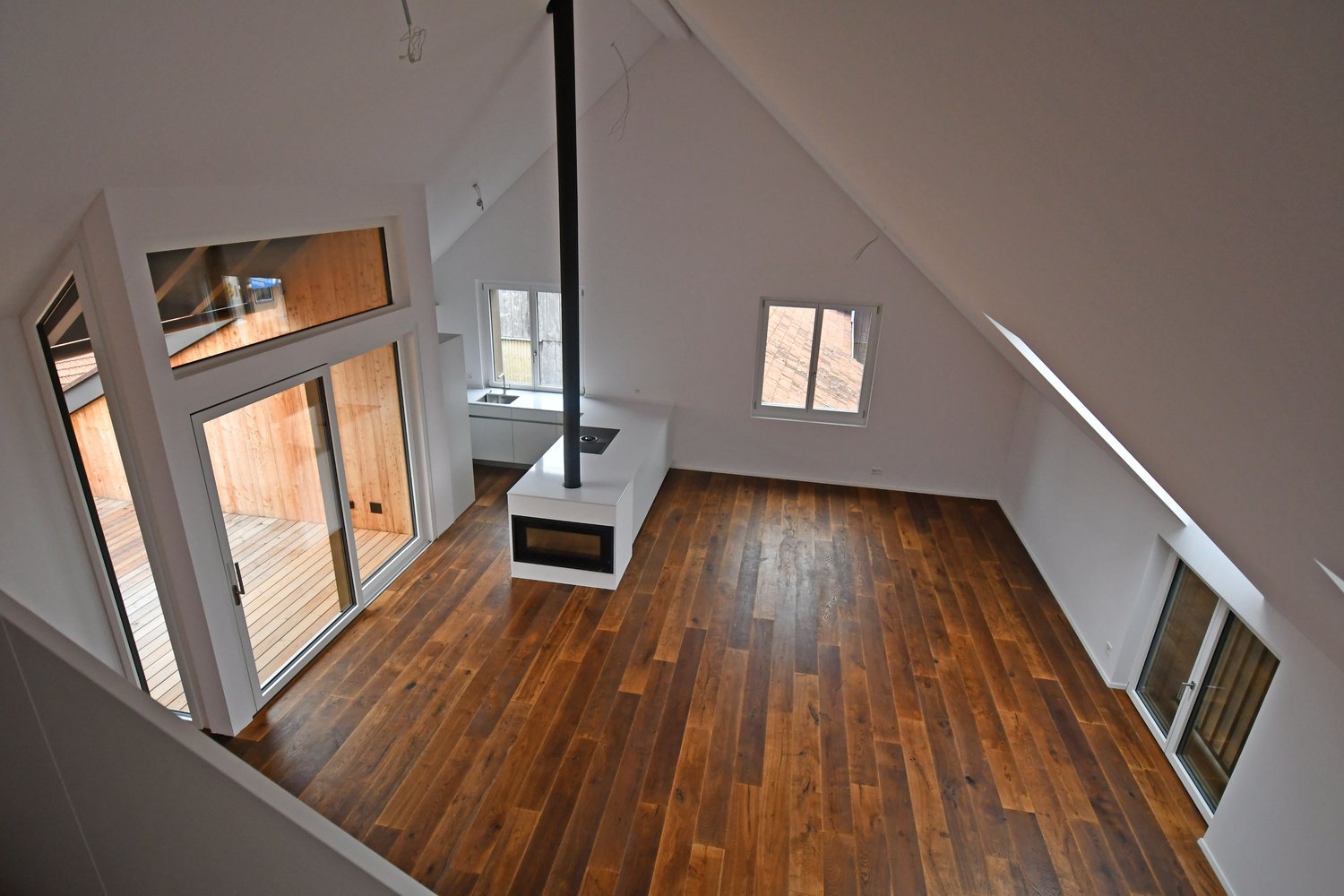 Interior view of an attic space with wooden flooring, glass doors, and windows.