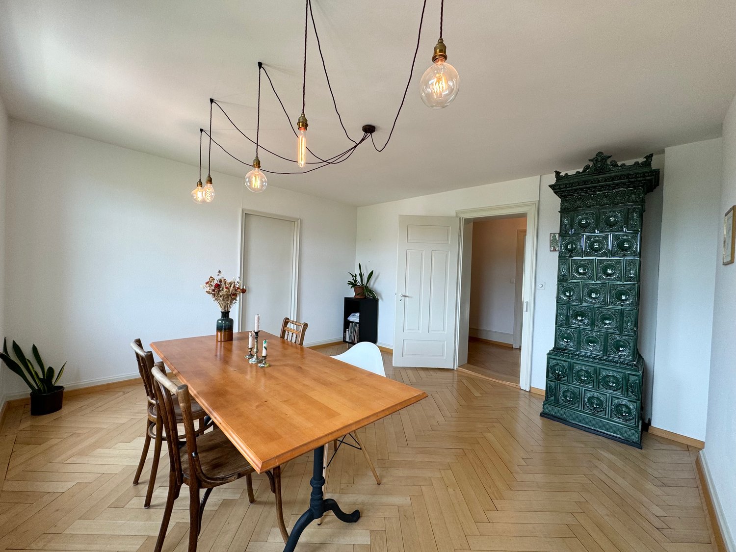 wooden dining table with chairs, wooden flooring, white walls, flower vase, vintage chandelier