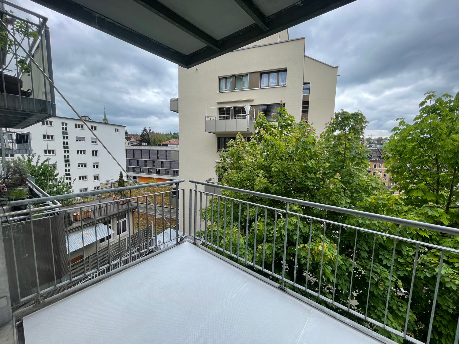 Outdoor balcony with metal railings, tiled floor, distant building views
