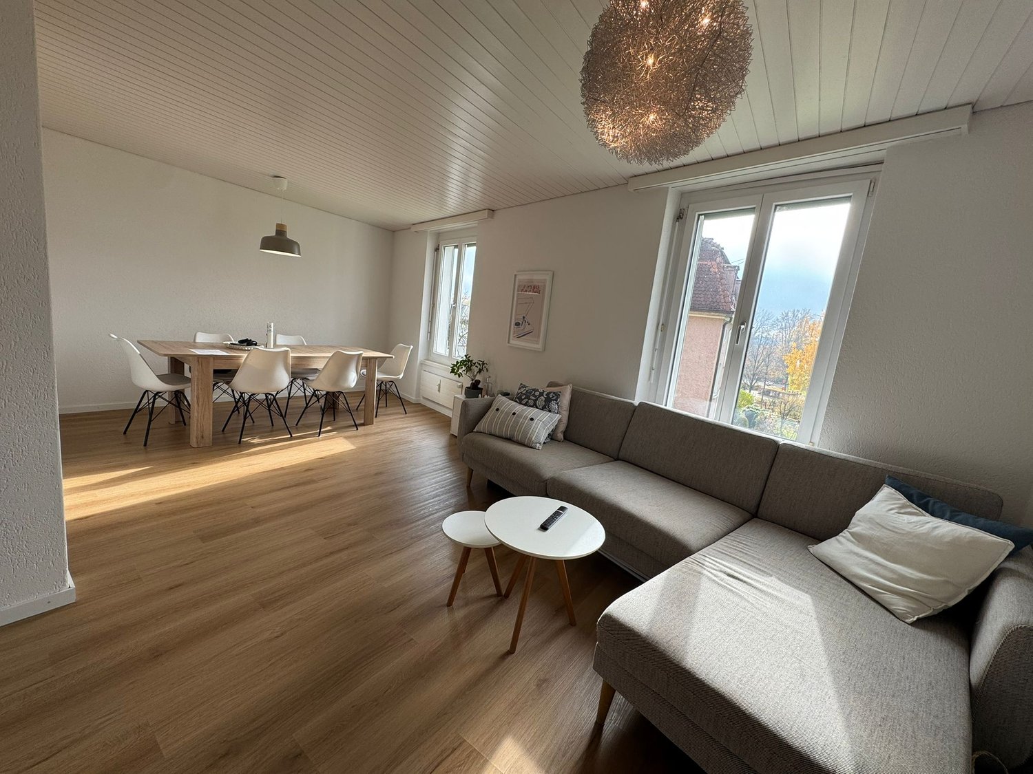 open living room with dining area, wooden floor, large windows, modern couch, coffee tables, lamps, view of the city