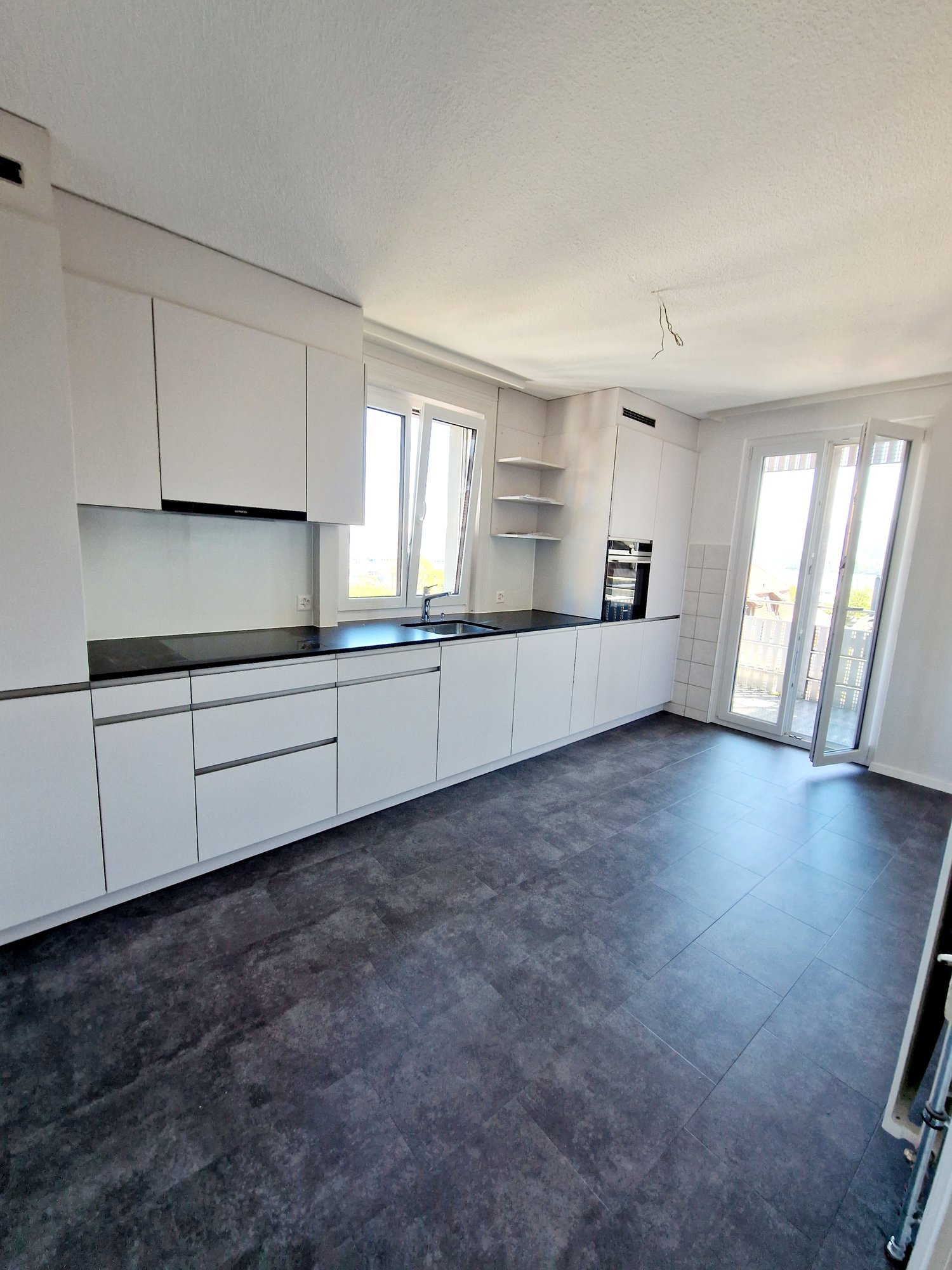 modern kitchen, white cabinets, black countertops, gray tiles, double windows, balcony door