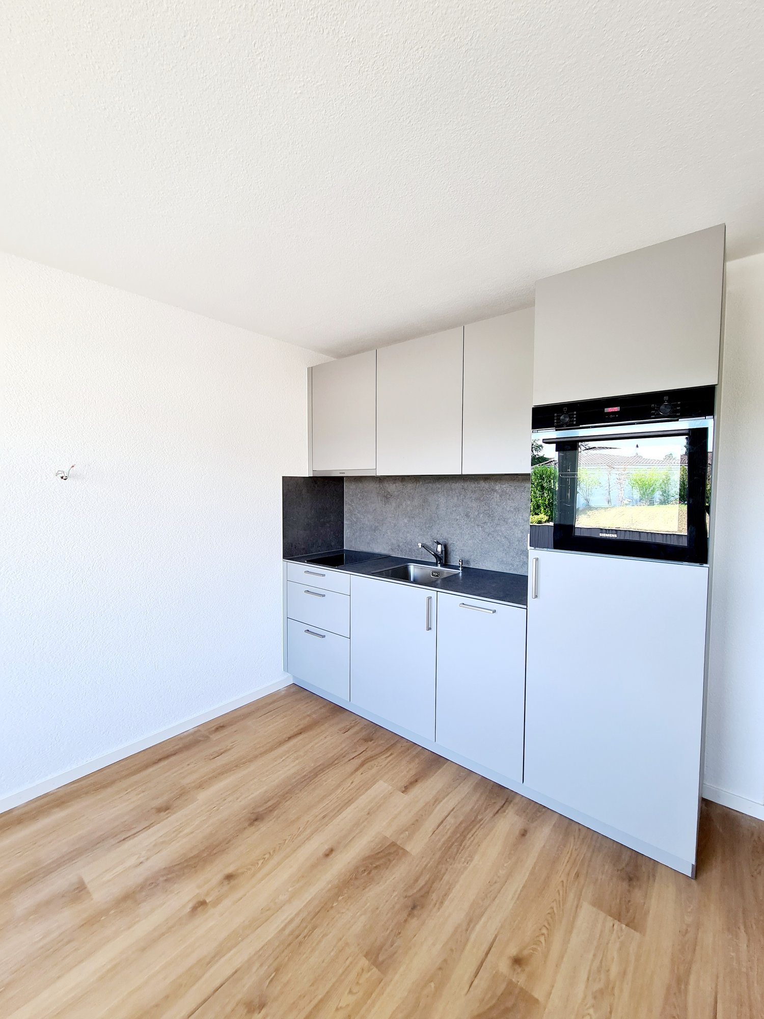 Modern kitchen with white cabinets, black countertop, built-in oven, and hardwood flooring