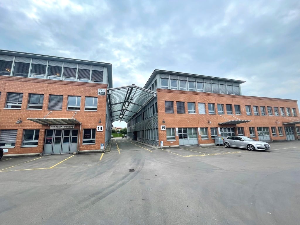 Multi-story commercial building with brick and glass facade, parking spaces in front, numbered entrances