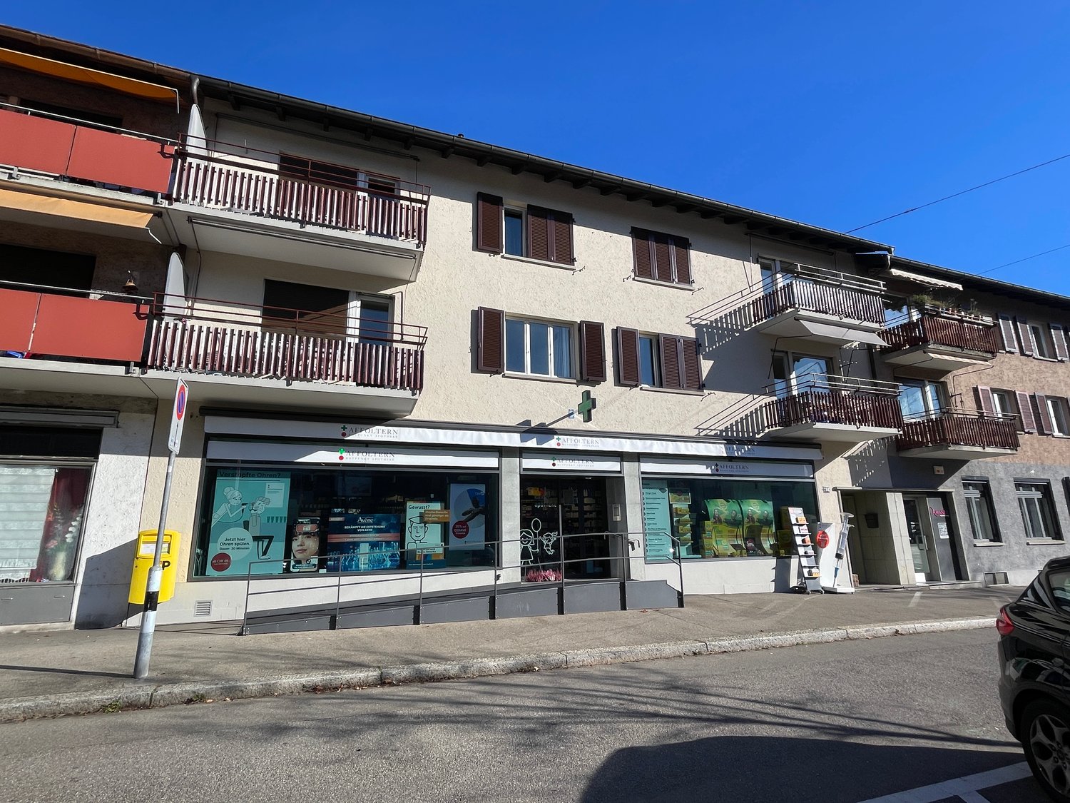 3-story building, balconies, red railings, awnings, shop on ground floor