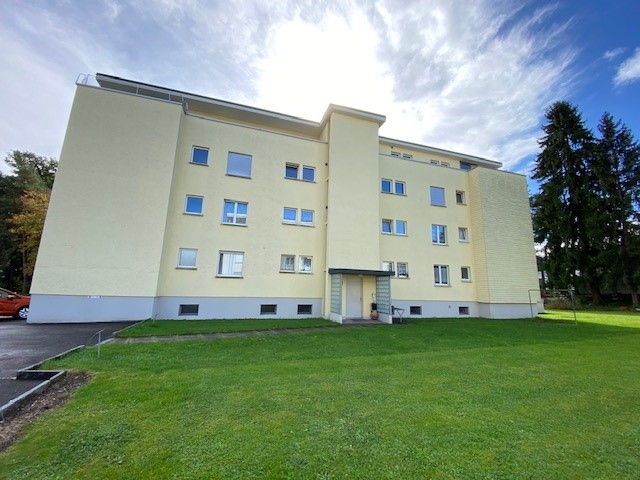large yellow building, 3 floors, multiple windows, garage, large lawn in front