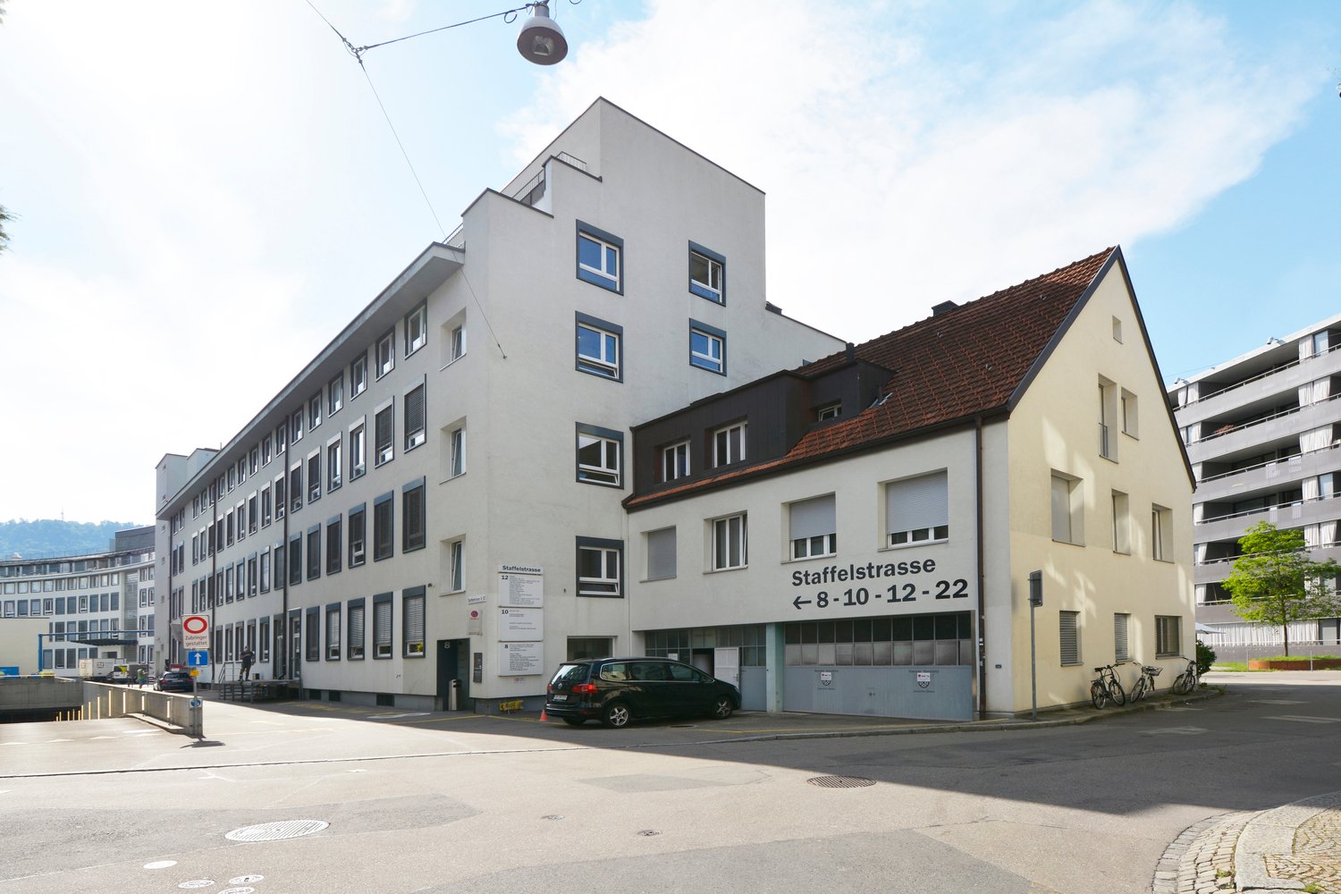 White building, brick roof, 4 floors, glass windows, car parked in front