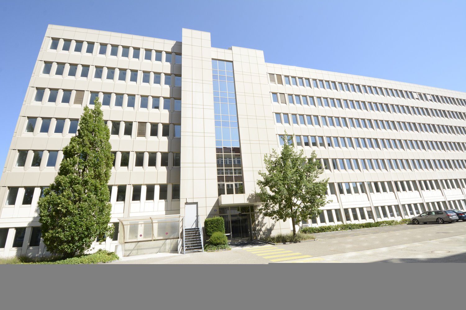modern office building, multiple floors, glass windows, entrance with staircase, parking area, two cars parked