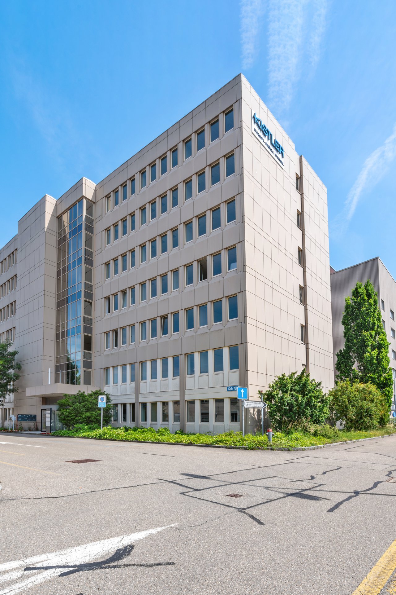 An office building with multiple stories, glass windows, a sign reading 'KISTLER' on the front facade, surrounded by greenery and a parking area.