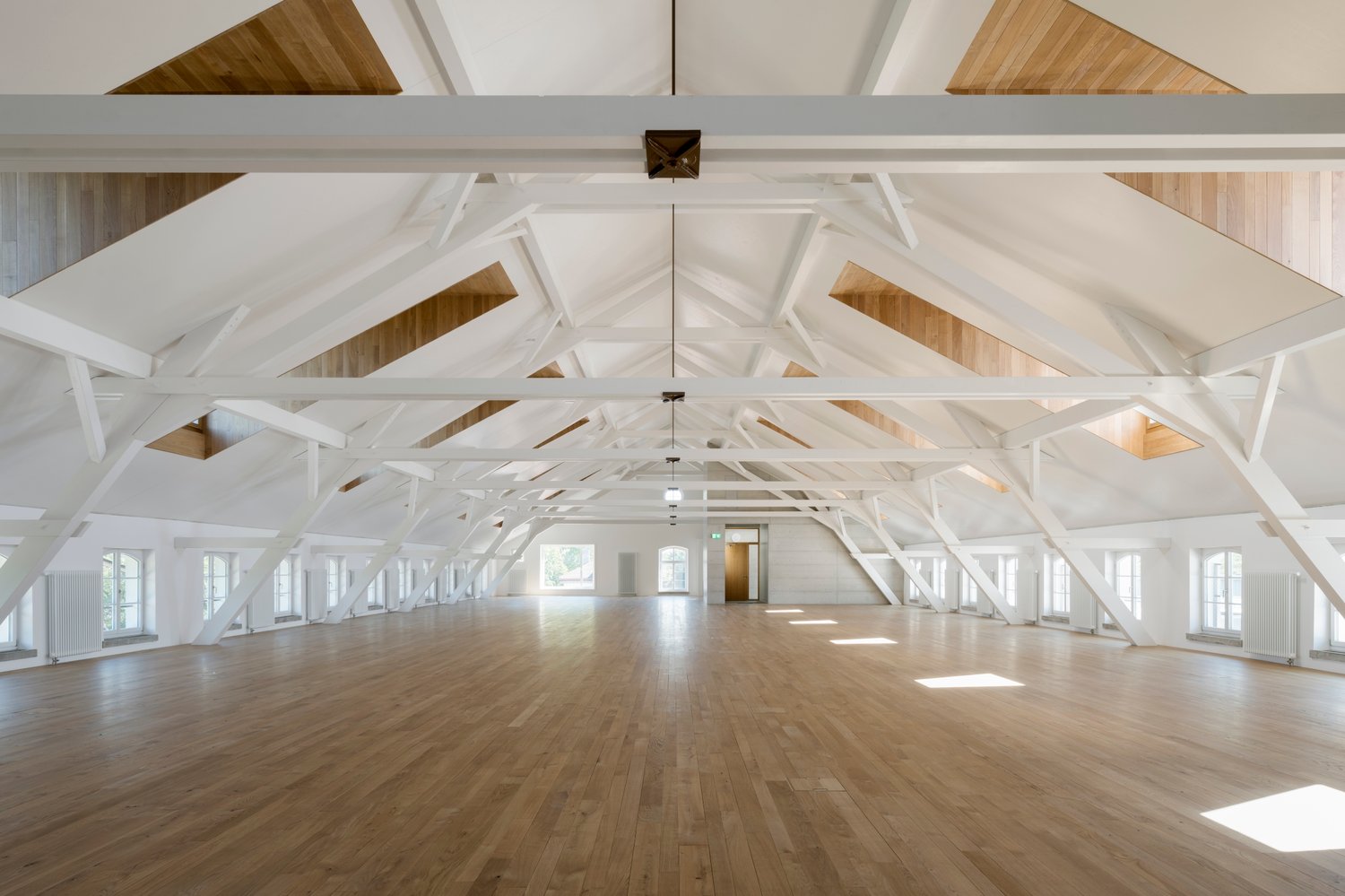 large open space, wooden floor, white walls, white beams, windows, wooden ceiling