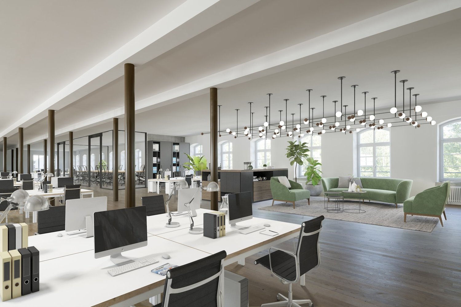 Modern office space with rows of desks and computer setups, contemporary lighting, a small couch area, and greenery