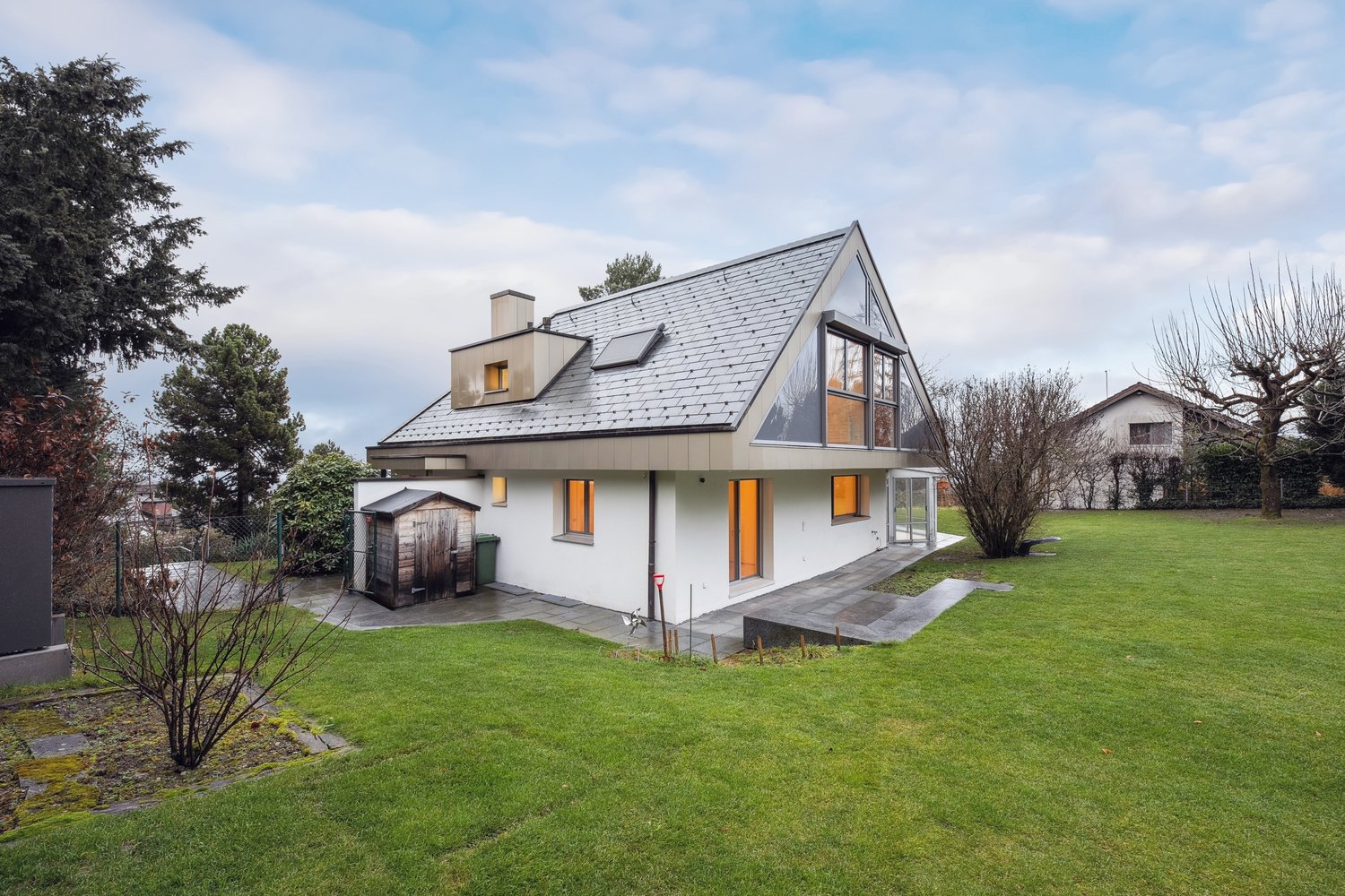white single story house, gray roof, large windows, exterior storage shed, paved driveway, grassy lawn