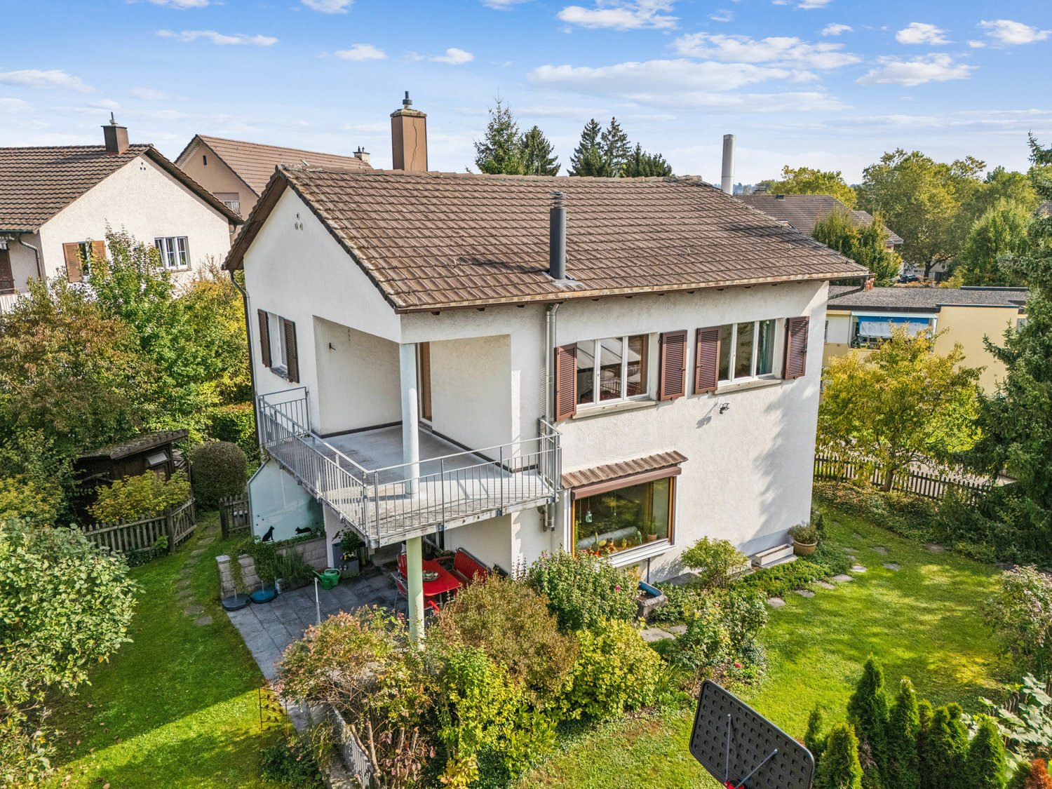two story house, white exterior, brown roof, balcony, garden with patio, dining table, red chairs