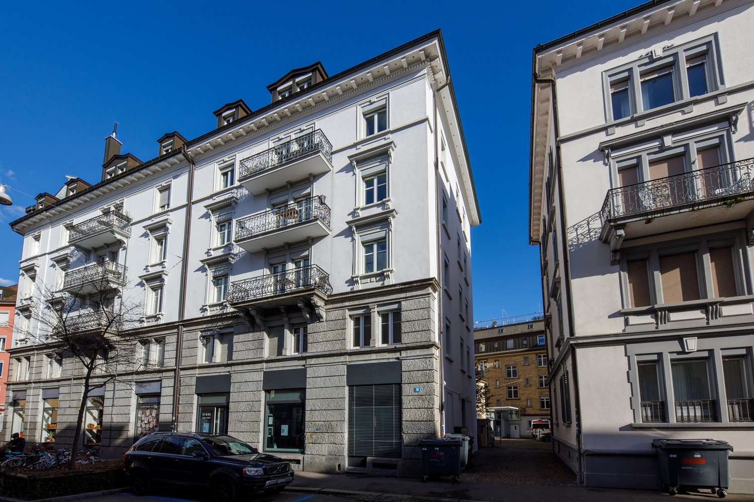 5 story building, balconies on each floor, gray exterior, white windows, parked car in front