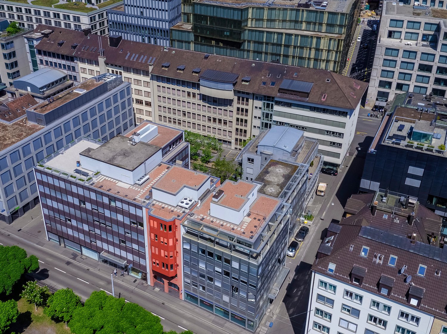 Urban area with multiple buildings, multistory parking, solar panels, various roof types, trees, street traffic
