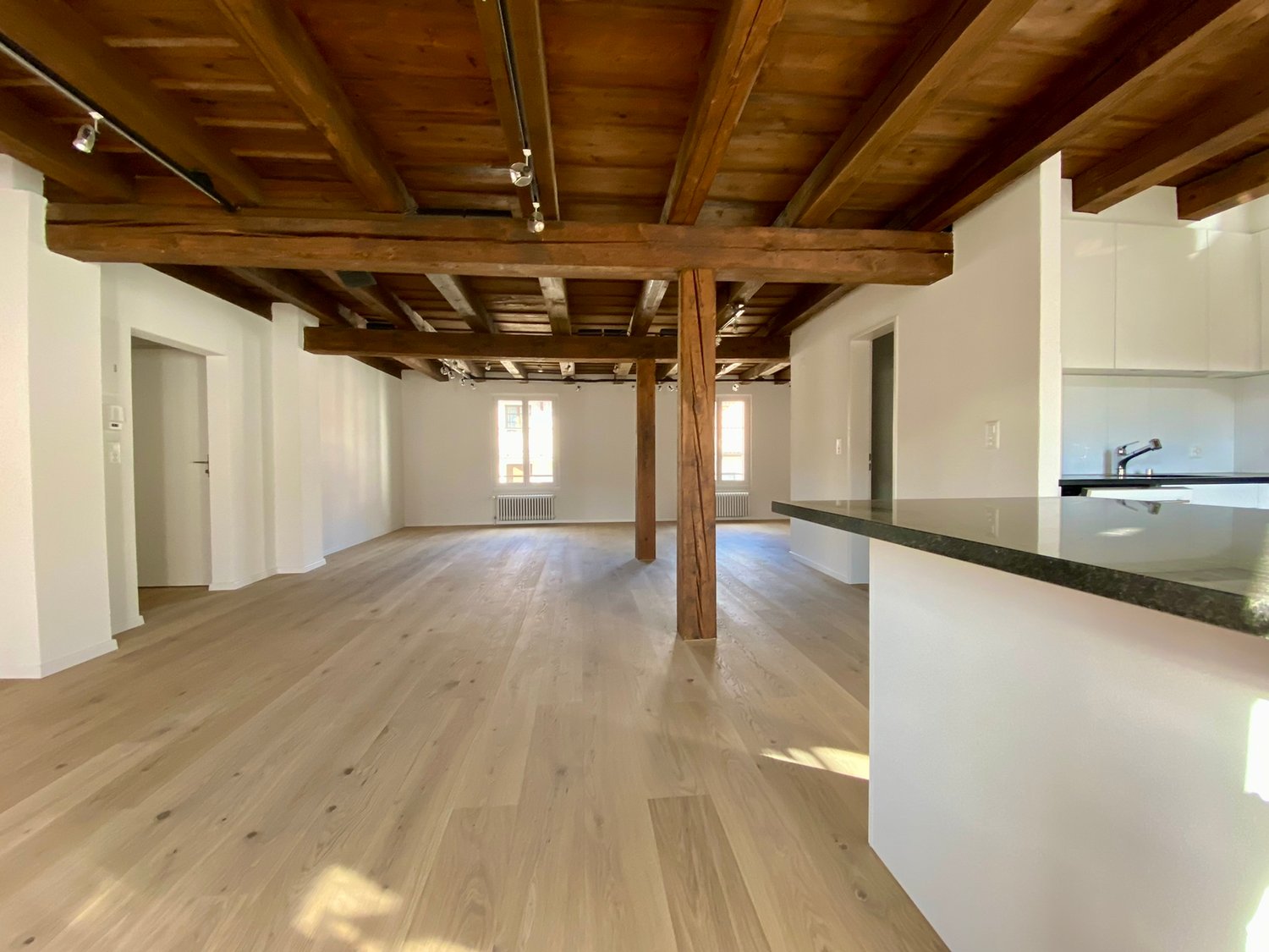 large open space, hardwood floors, exposed wooden beams, modern kitchen area with countertop