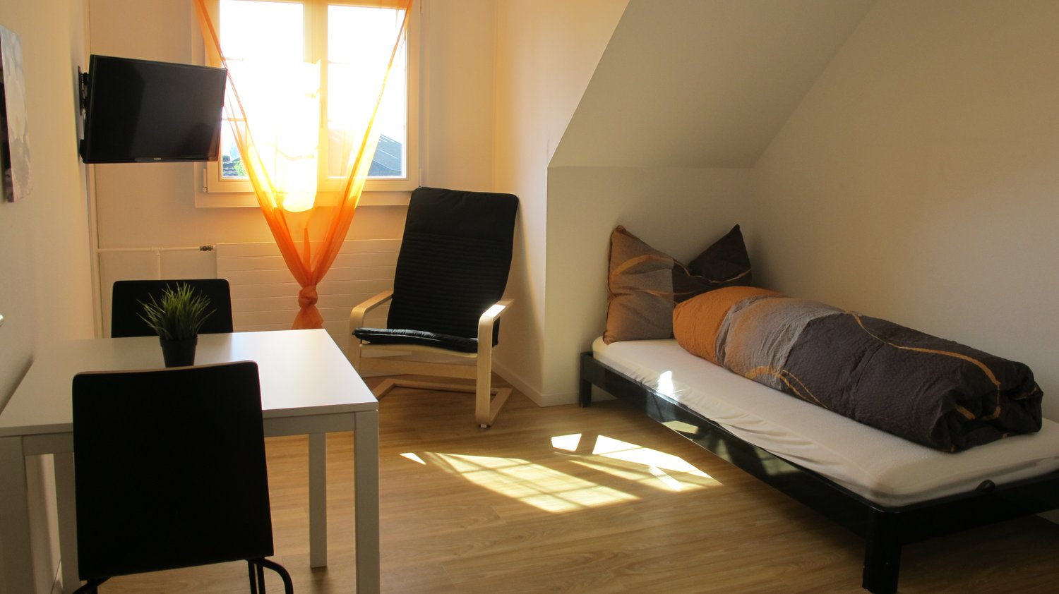 Bedroom with bed, table, TV, and window with curtain.