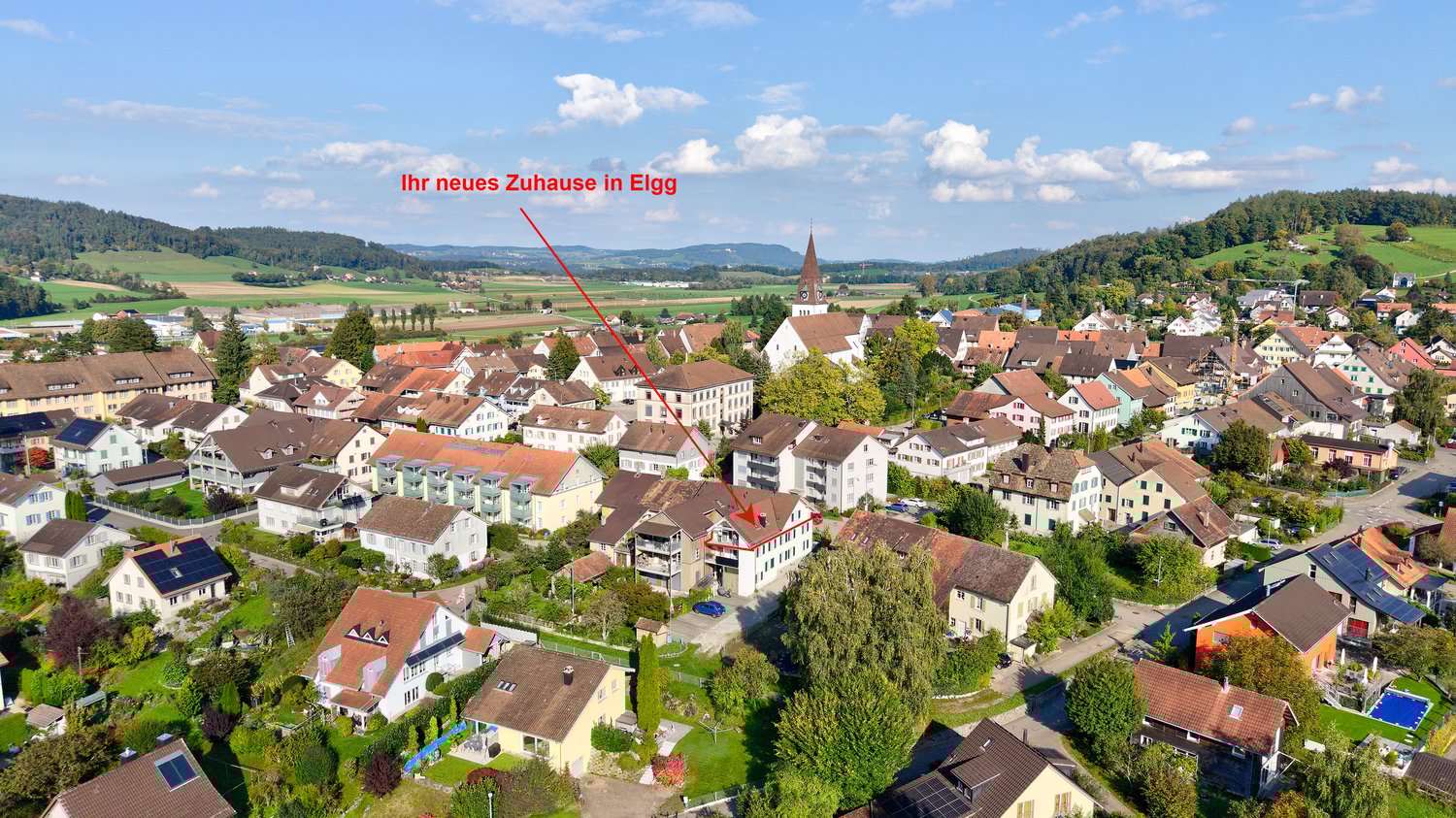 House located in Elgg, Switzerland, marked by a red arrow, situated among other houses in a residential area with a church in the background.