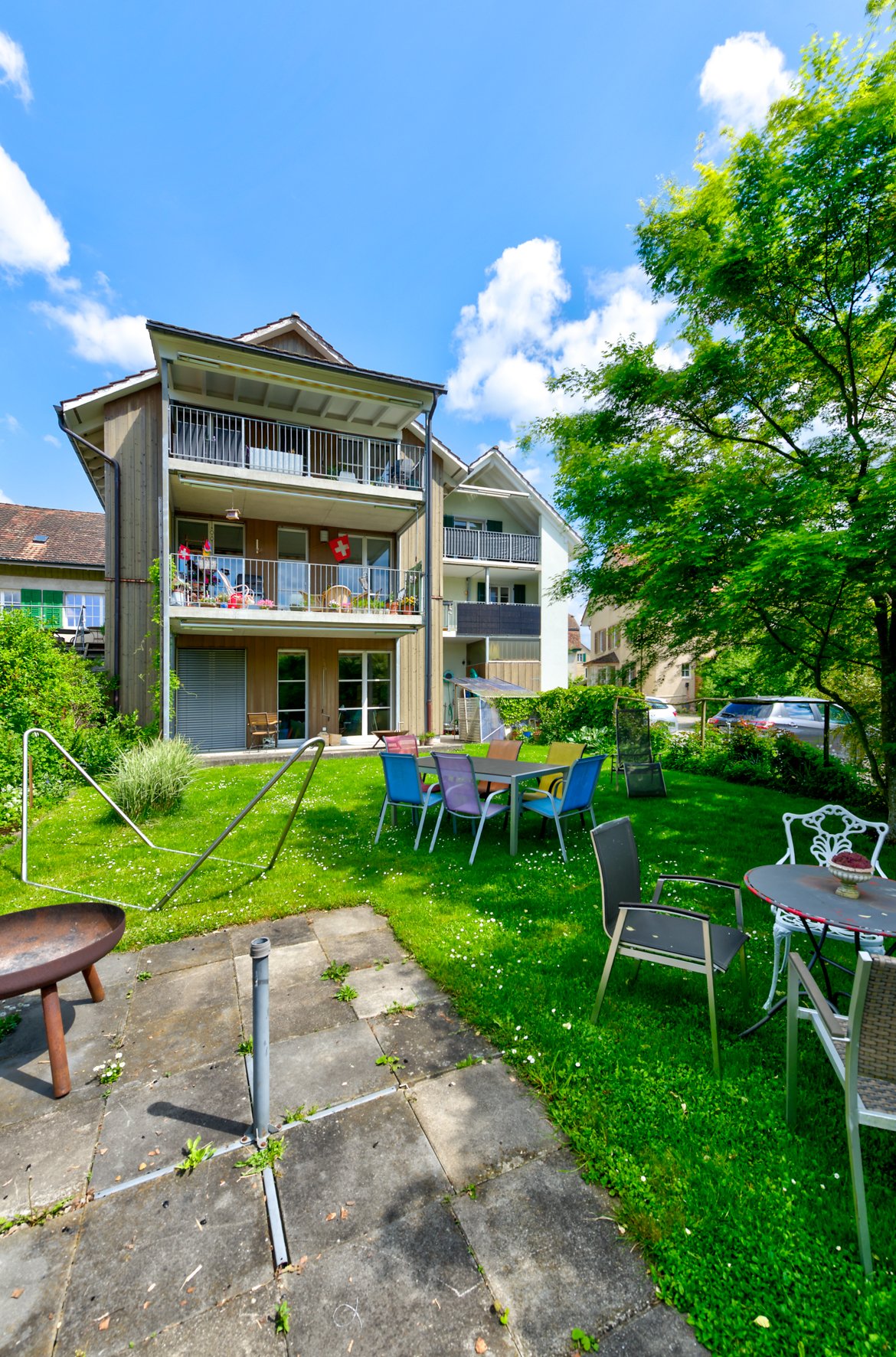 3 story apartment building, balconies, large lawn with tables and chairs, open canopy