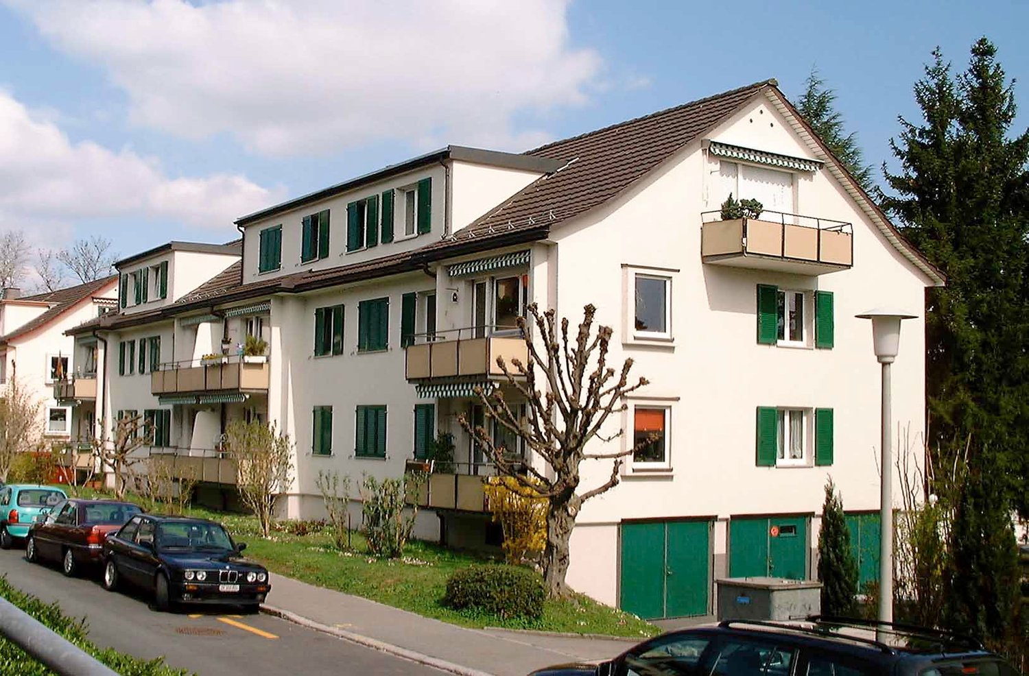 3-story building with white exterior, green shutters, multiple balconies, garage doors at the base, street level parking