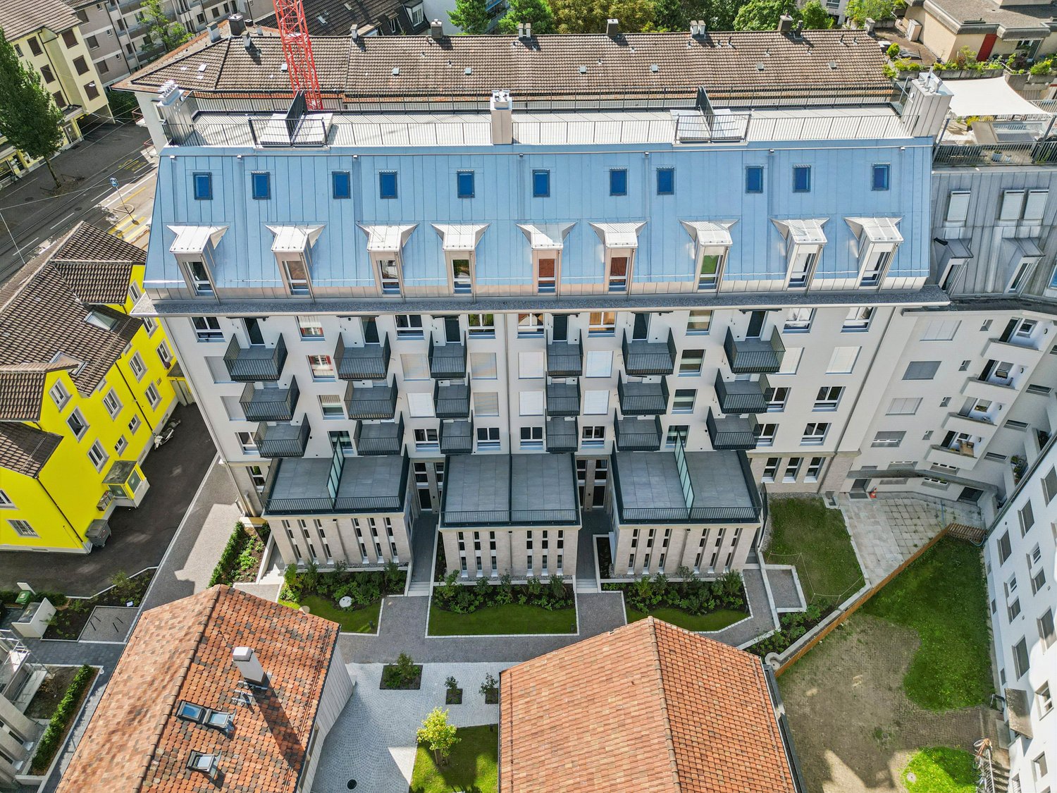 Modern apartment building with blue roofing, several balconies, landscaped gardens and parking