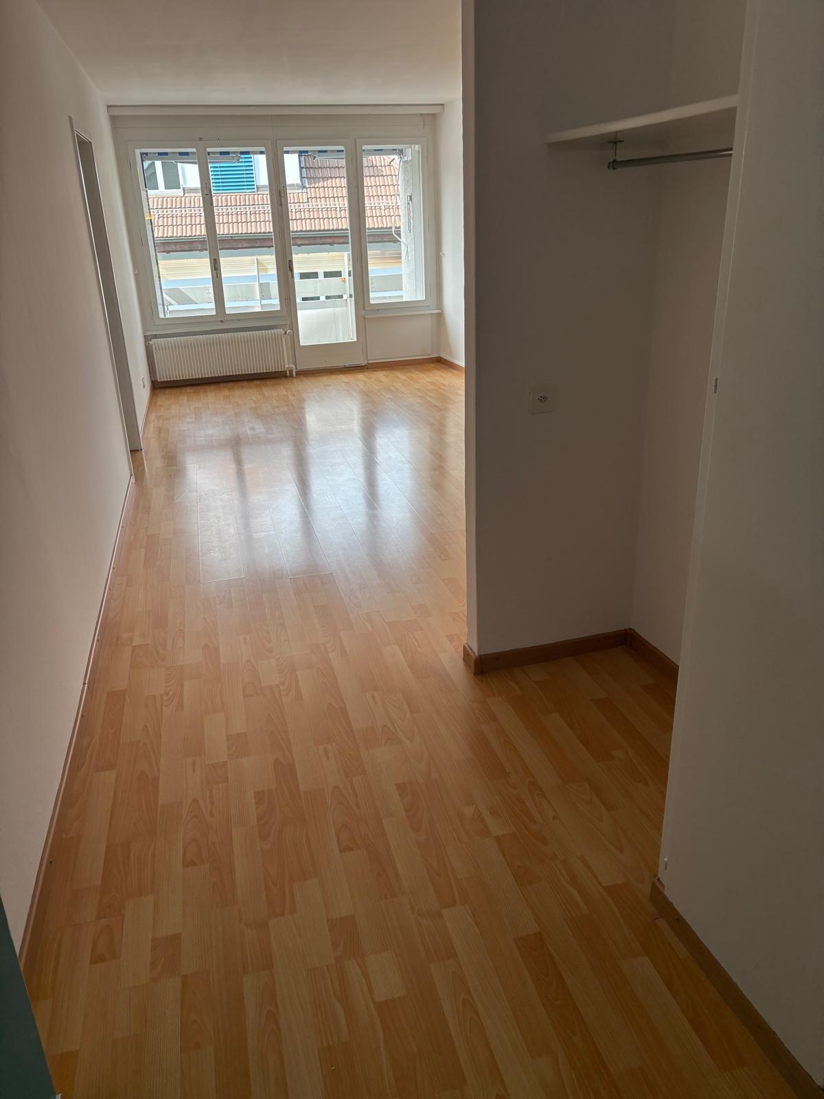 Empty room with wooden floors, glass windows, a white wardrobe, a window sill with a white radiator, white walls