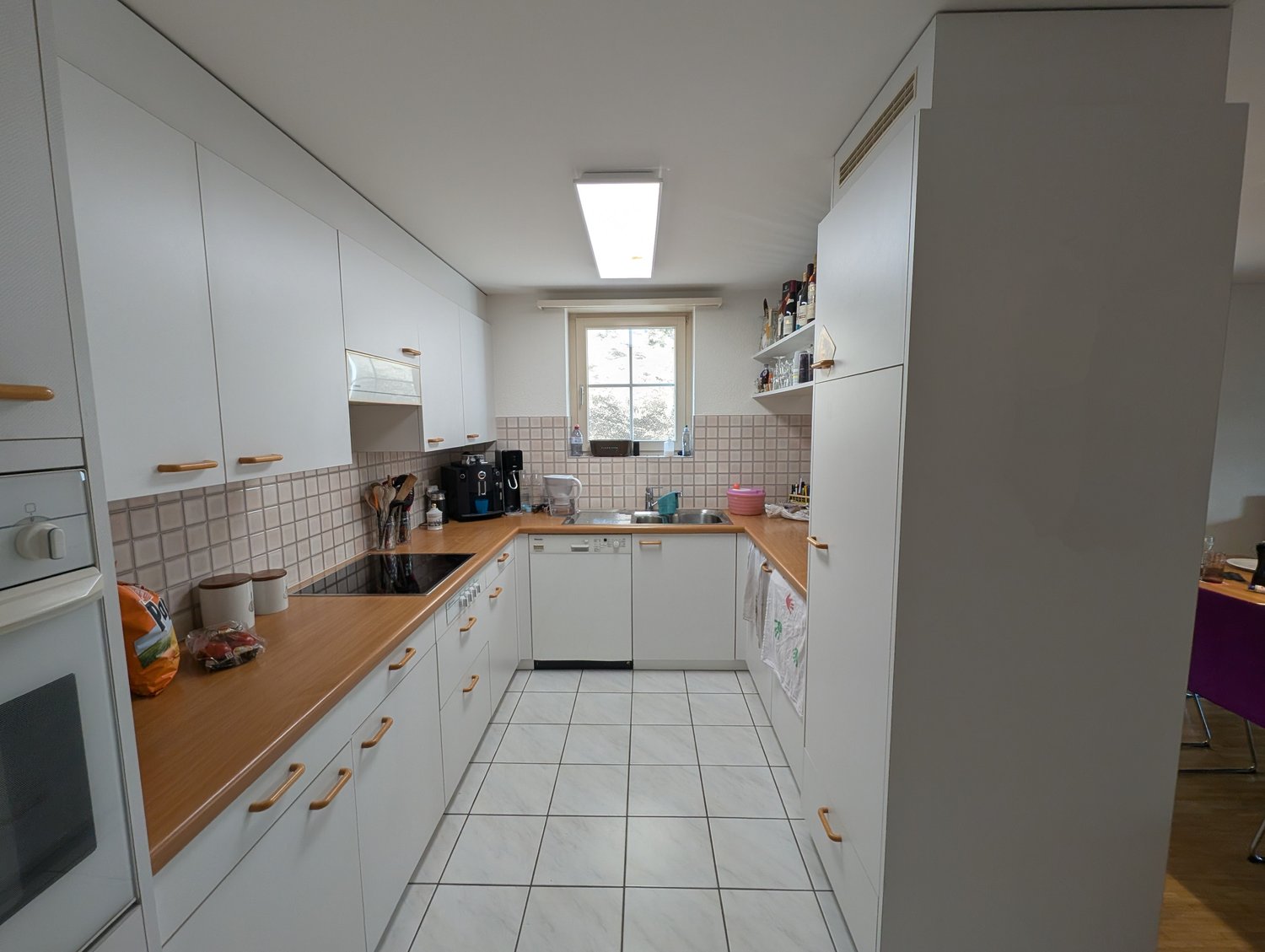 Galley-style kitchen with white cabinets, wooden countertops, tiled floor, and a dishwasher visible