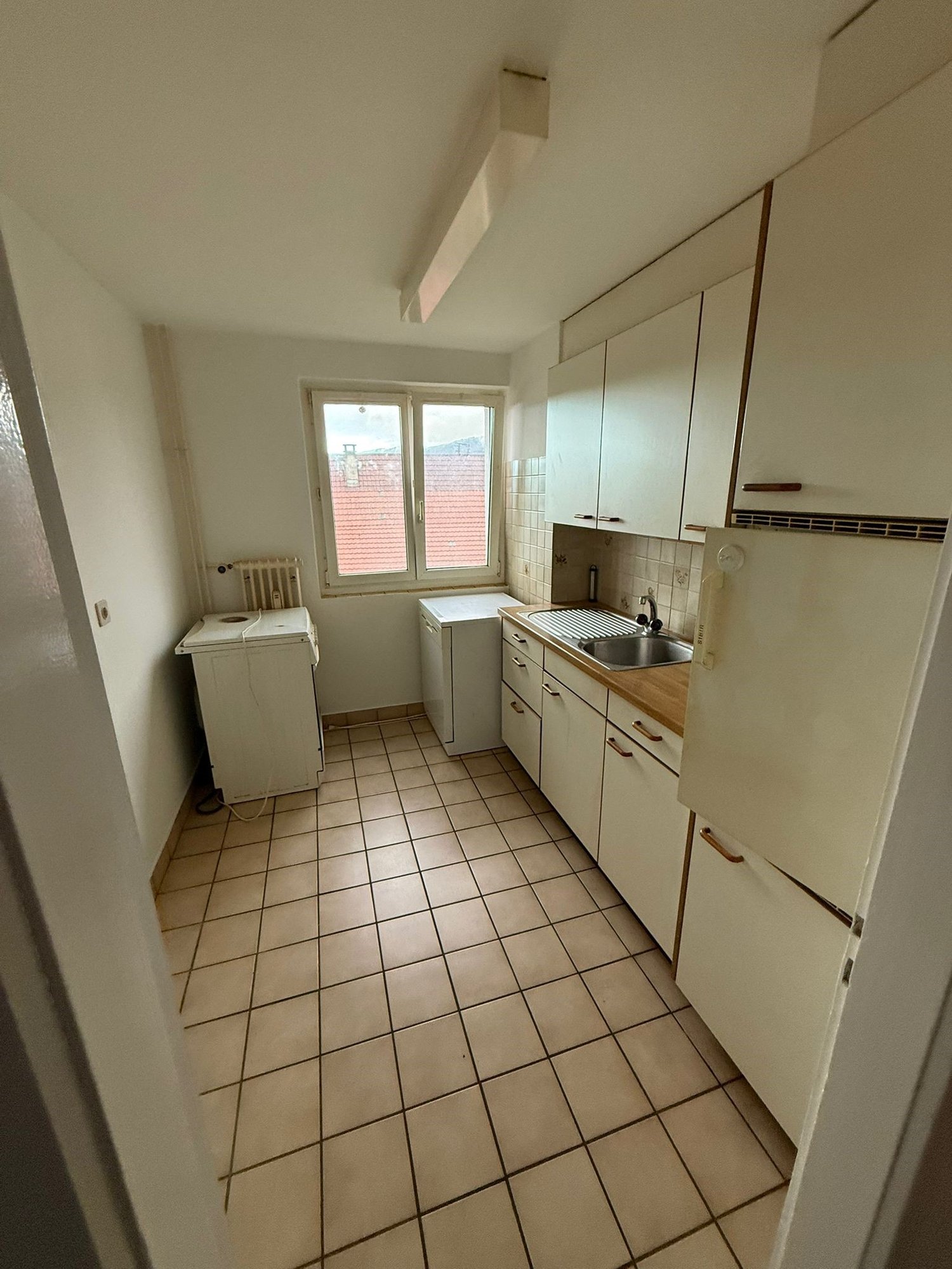 Clean kitchen with tiled flooring, white appliances, window, sink, and countertop