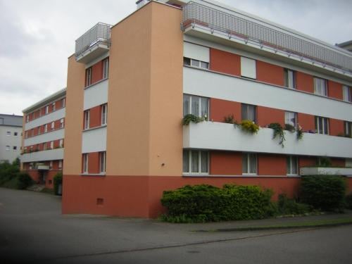 5 story building, orange and white, balcony, windows, front area with plants