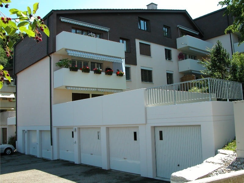 Multi-story building, white walls, balconies, attached garages, garden
