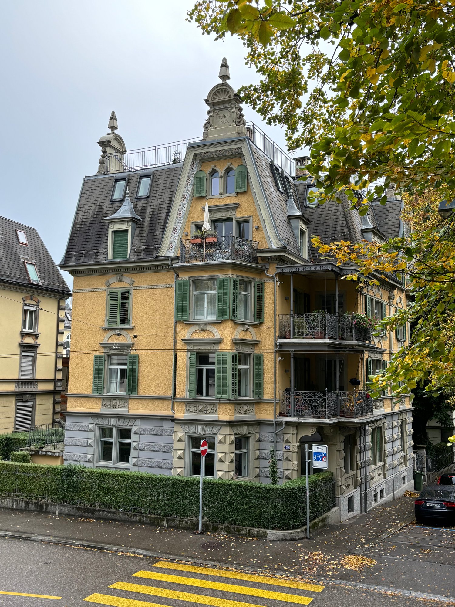 Multi-story building with balconies, yellow exterior, intricate architectural details, multiple windows, surrounding greenery
