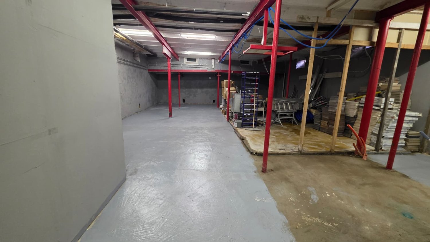 empty basement, gray concrete floor, red beams, scattered items and materials