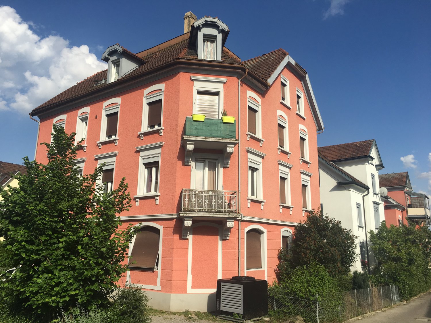 A multi-story residential building with a red exterior, ornate architectural details, and a balcony on the upper floor.