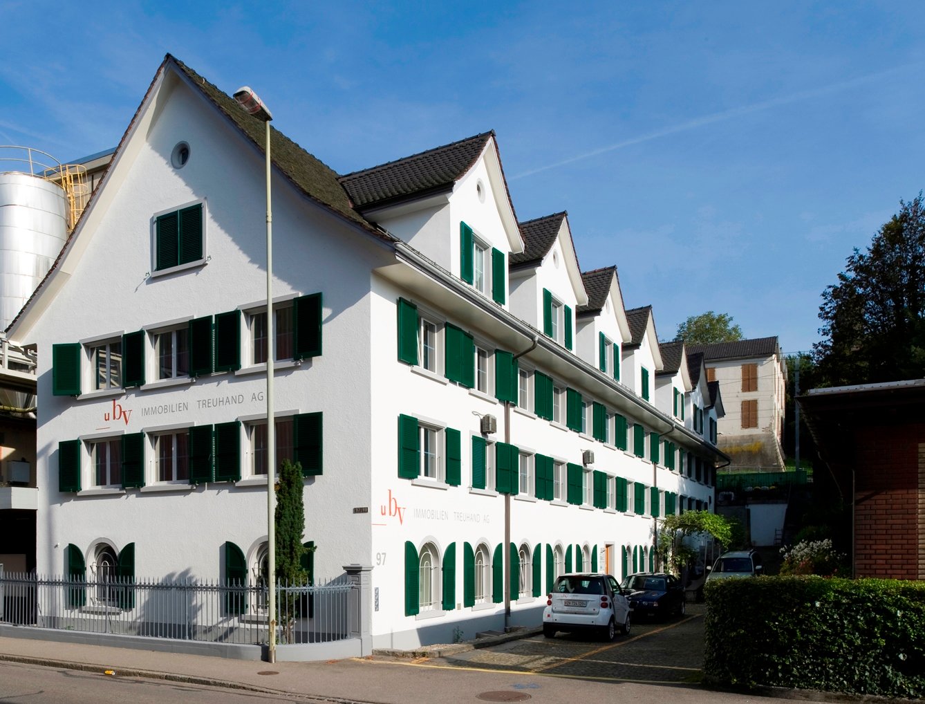 white house, green shutters, three stories, metal fence, 4 windows in the first row, 5 windows in the second row, 4 windows in the third row