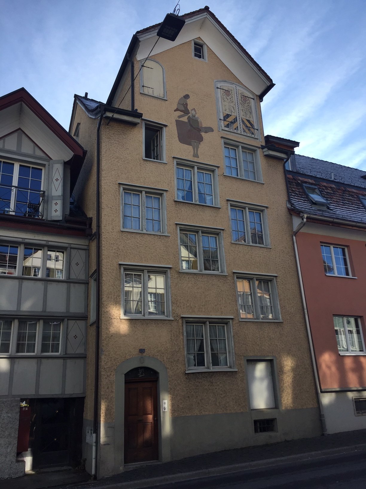 A four story residential building made of bricks, a balcony with an awning, windows with shutters