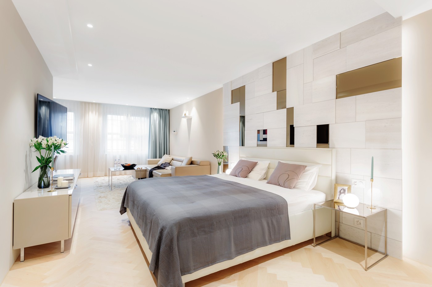 spacious bedroom with white walls, modern design, king-size bed, wooden floor, side table, TV, flower vase, couch