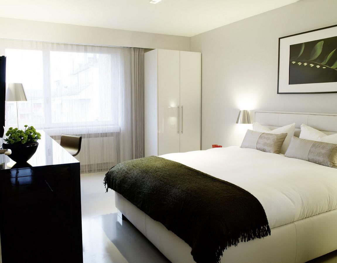 modern bedroom with a king size bed, white walls, large window, white cabinet, desk, white linens, plants