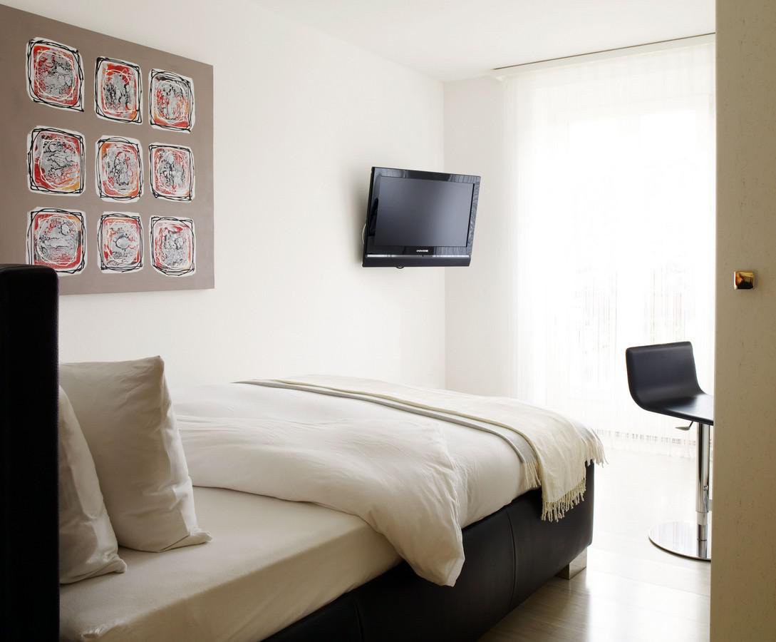 single bed, modern design, mounted TV, decorative painting, white pillow, black cushioned chair